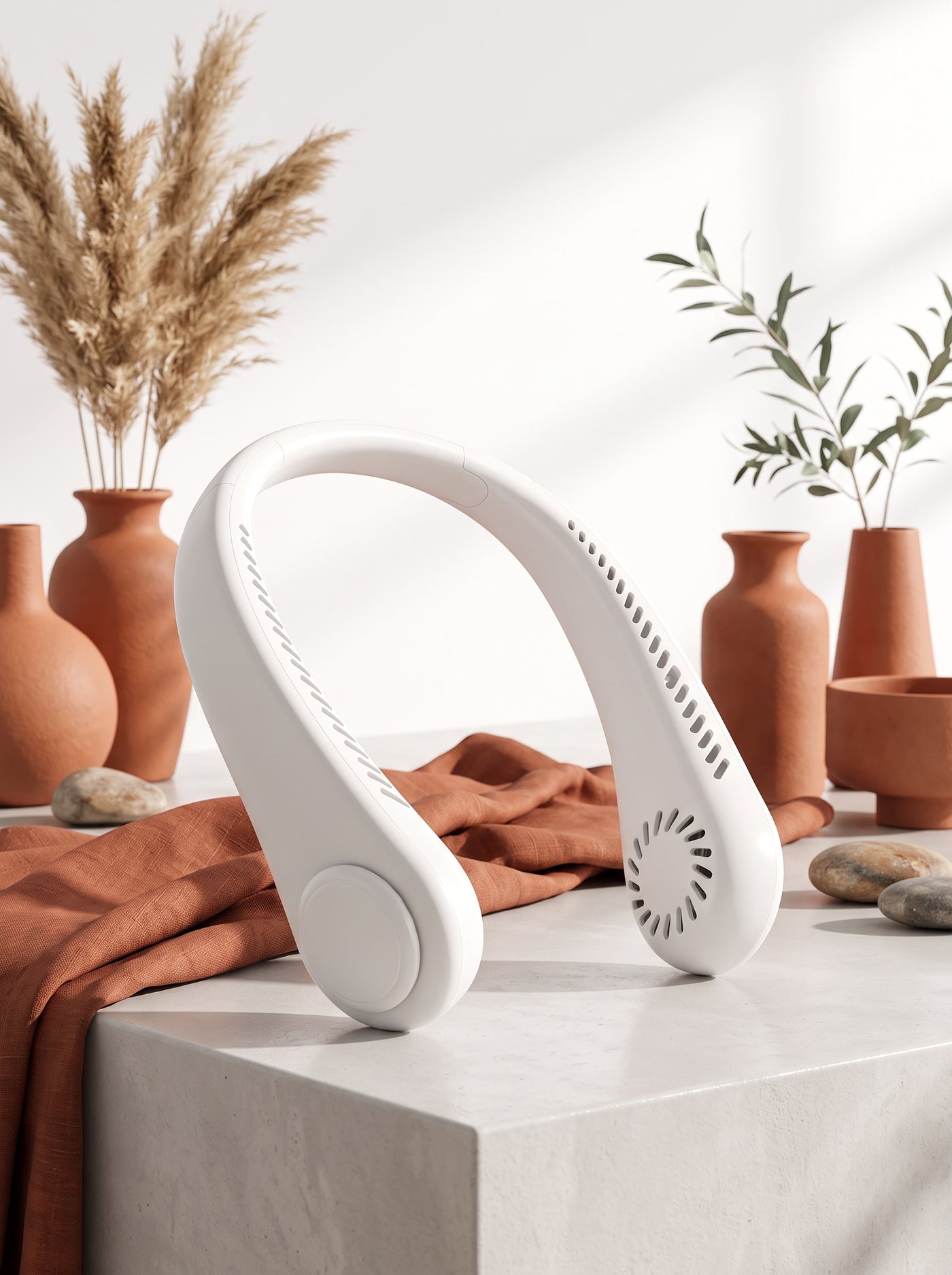 A white bladeless neck fan displayed on a minimalist surface with terracotta and burnt sienna decor in a bright, modern room.